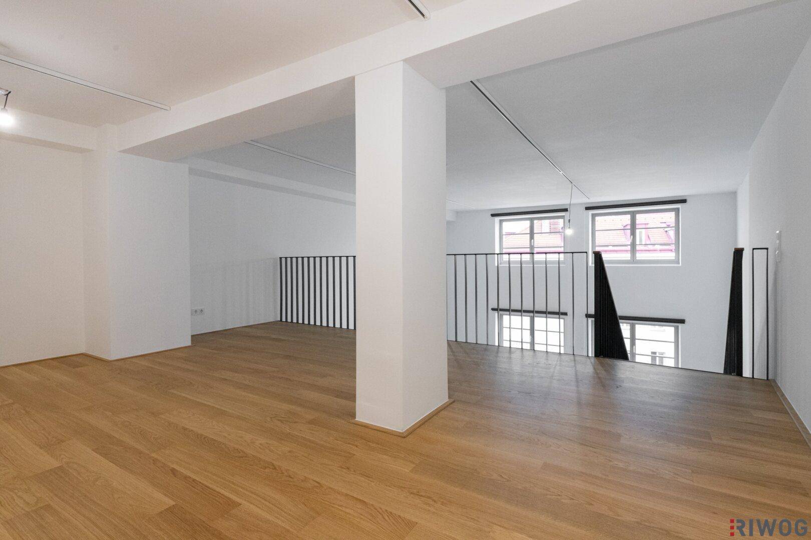 Helle Galerieebene mit Holzfußboden und Blick auf die unteren Fenster.