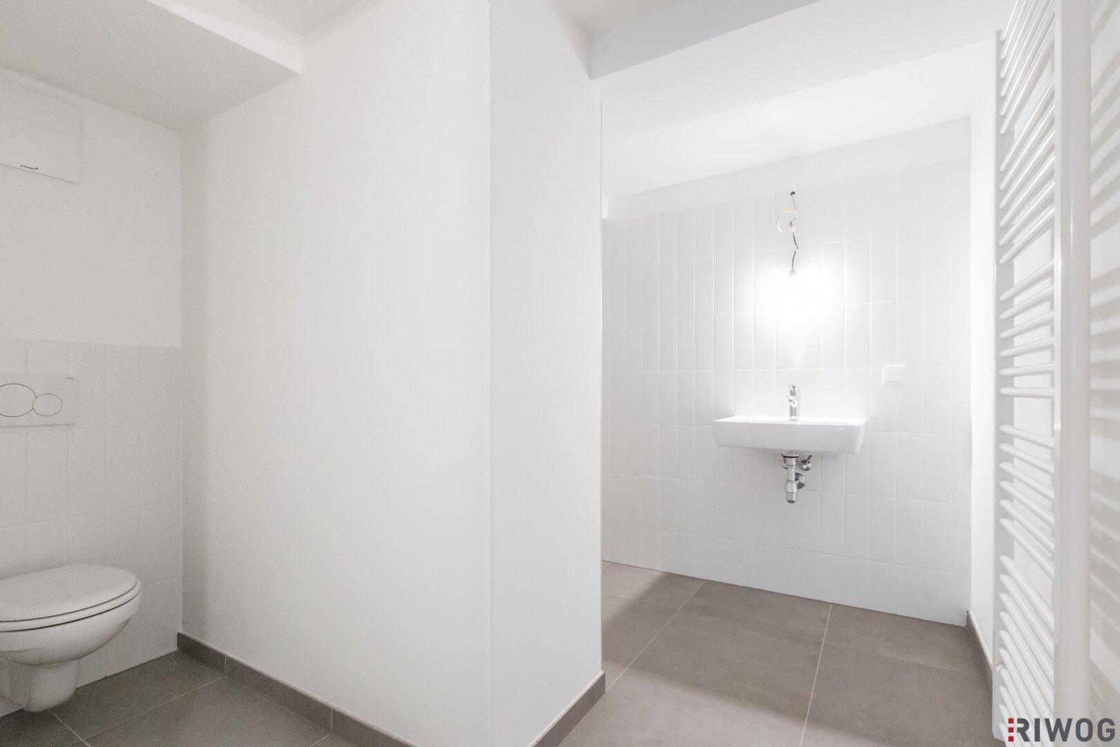 Modernes Badezimmer mit weißen Fliesen, Hänge-WC und Waschbecken.