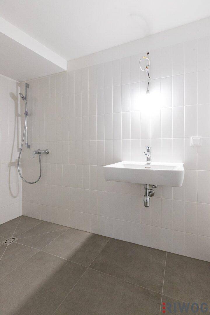 Helles Badezimmer mit ebenerdiger Dusche, modernem Waschbecken und weißen Fliesen.