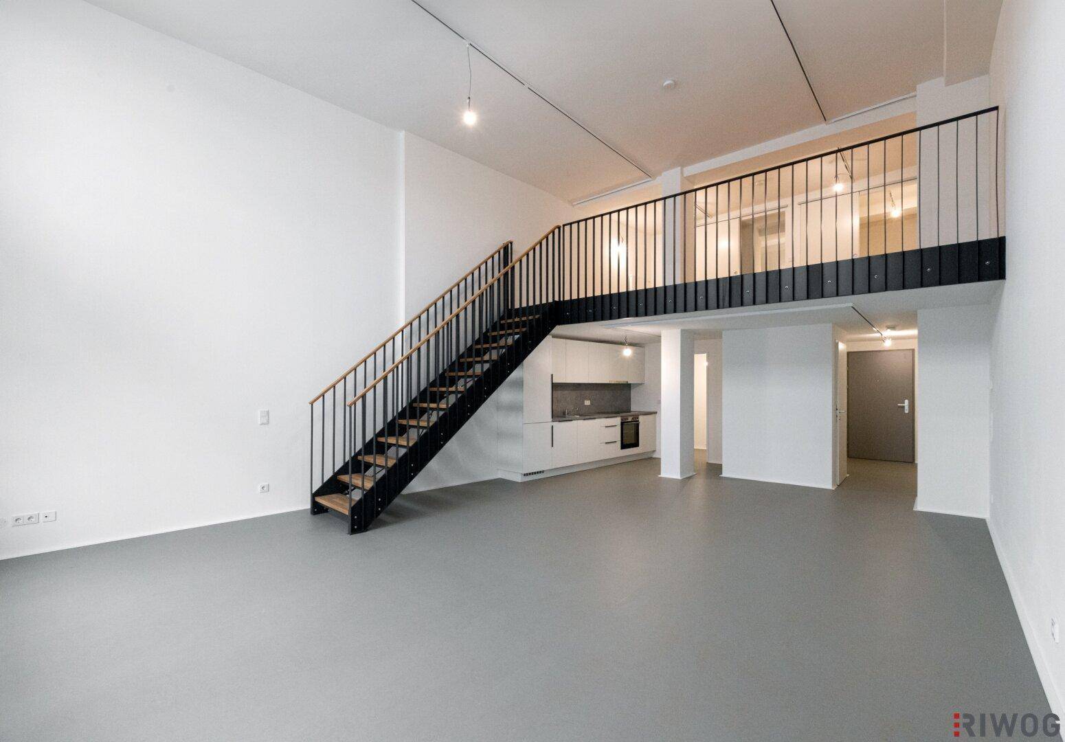 Heller Loft-Wohnbereich mit hohen Decken, Galerie und moderner Einbauküche im Hintergrund.