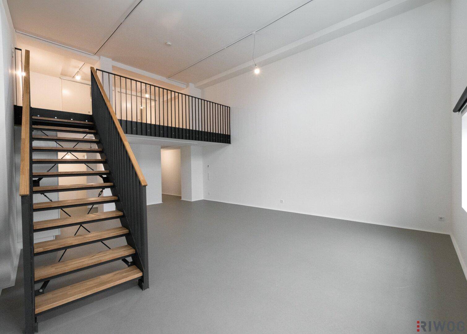 Geräumiger, unmöblierter Loft-Wohnbereich mit moderner Treppe zur Galerie.