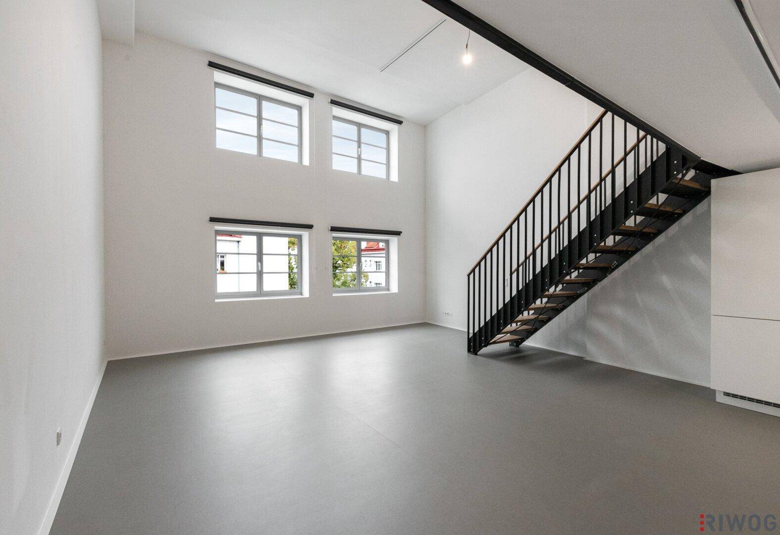 Lichtdurchfluteter Loft-Raum mit hohen Fenstern und Blick auf die Umgebung.