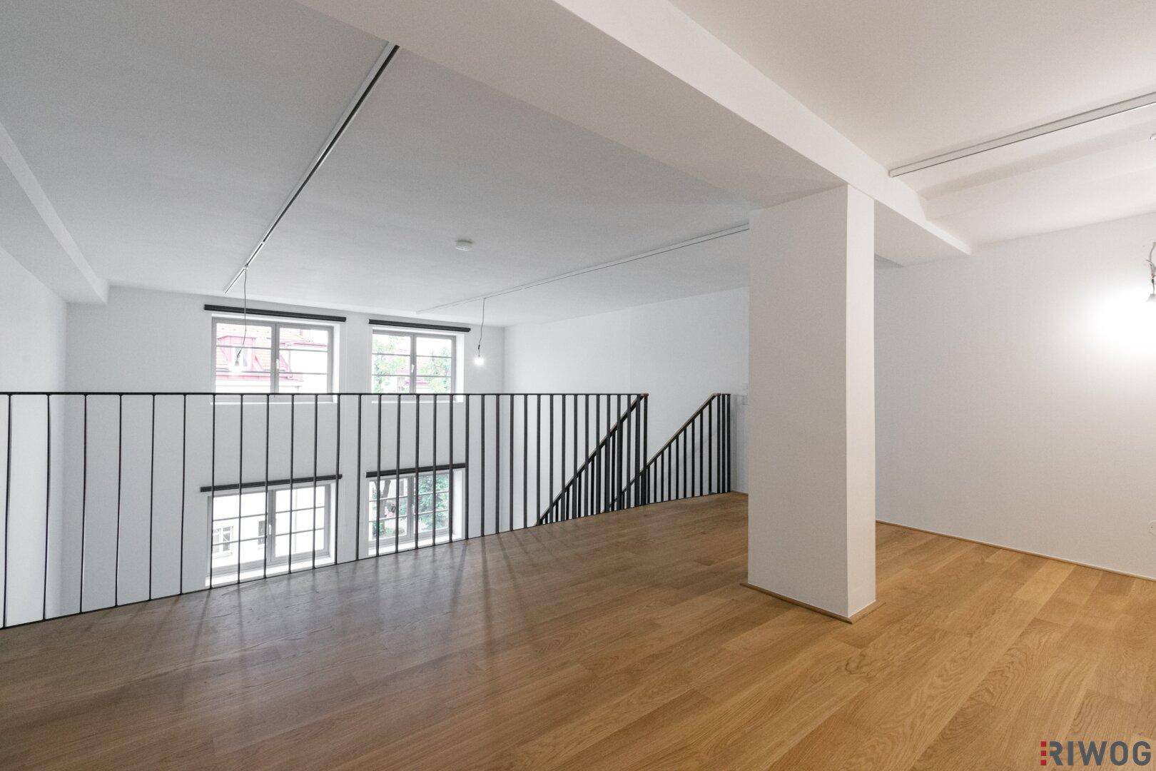 Geräumige Galerie mit Holzboden und Fenstern, die viel Tageslicht hereinlassen.