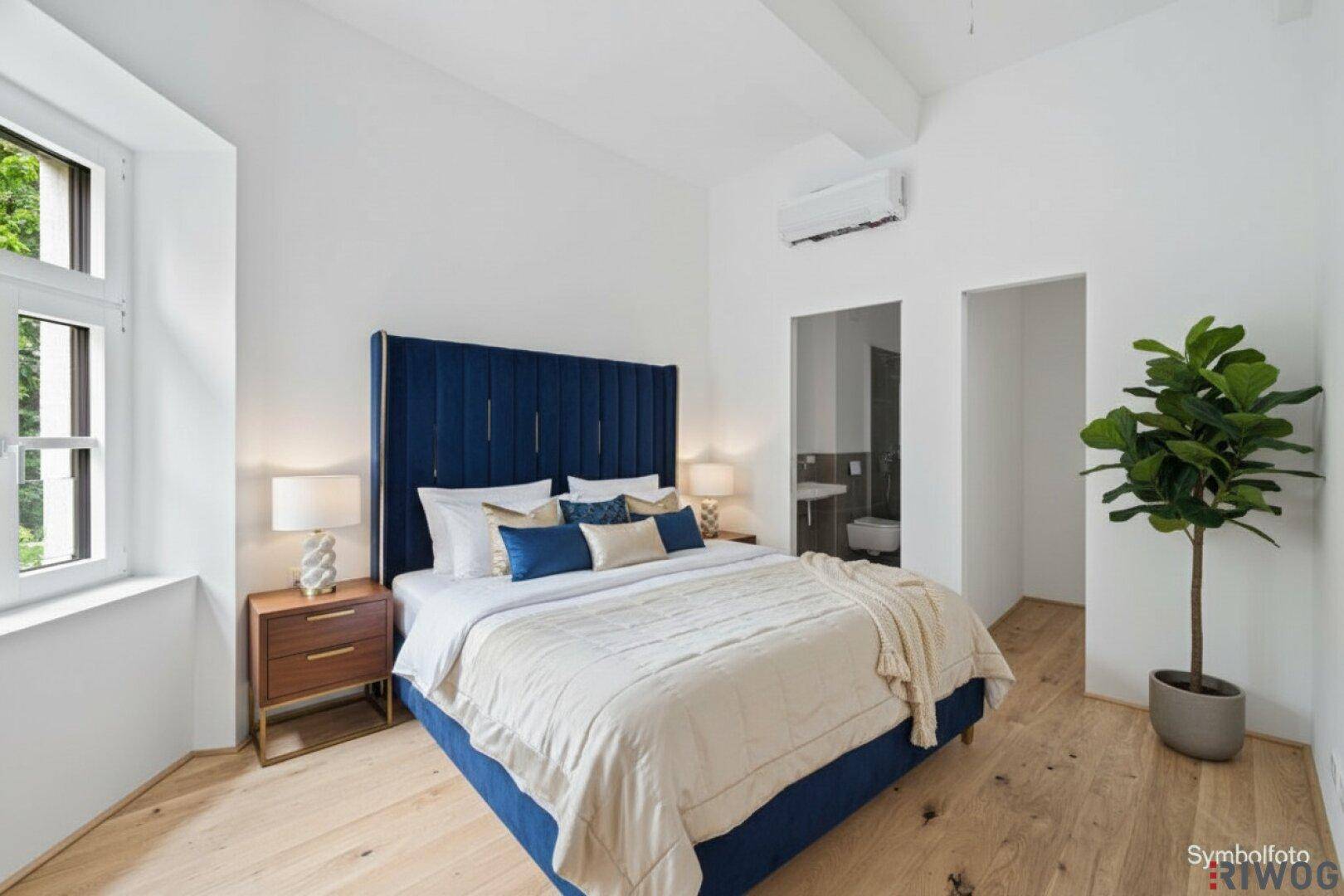 Gemütliches Schlafzimmer mit blauem Bett, Holzboden, Klimaanlage und Zugang zu einem angrenzenden Badezimmer.
