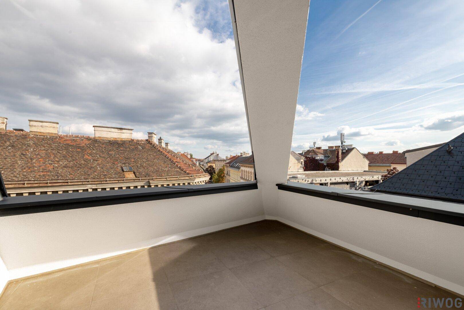 Geräumige Dachterrasse mit Fliesenboden und Panoramablick über die städtische Umgebung an einem sonnigen Tag.