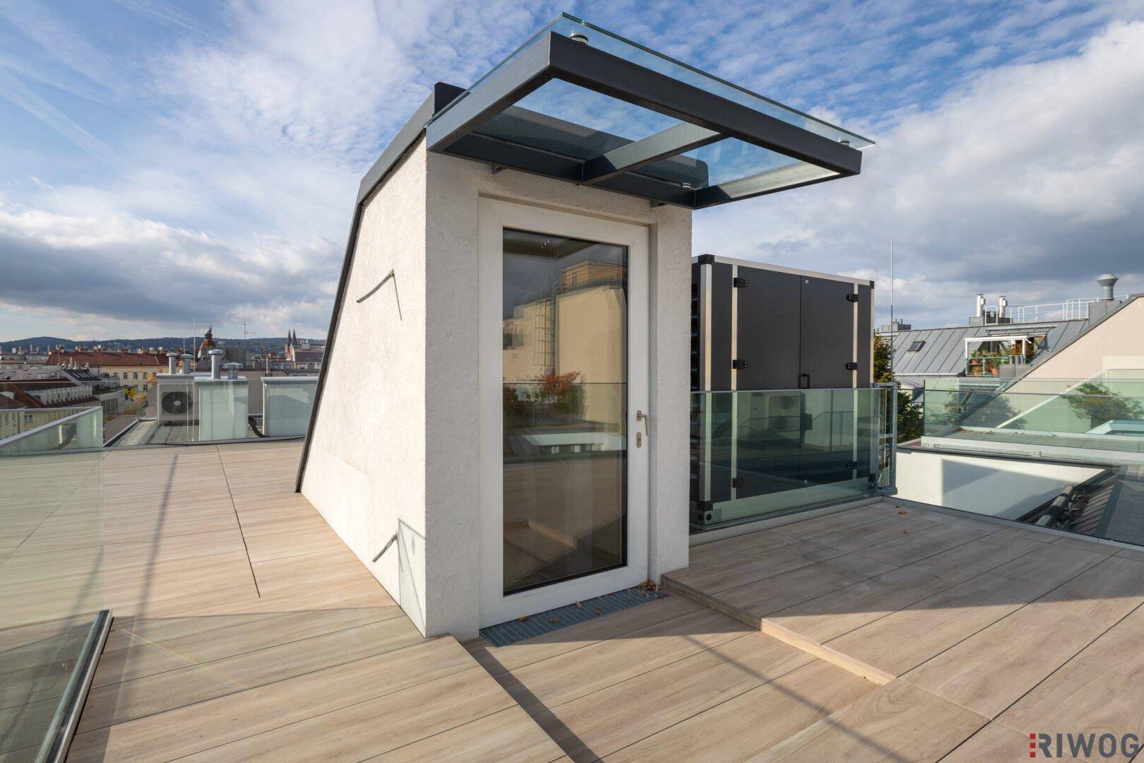 Moderner Dachausgang mit Glasüberdachung und Zugang zur Dachterrasse unter blauem Himmel.