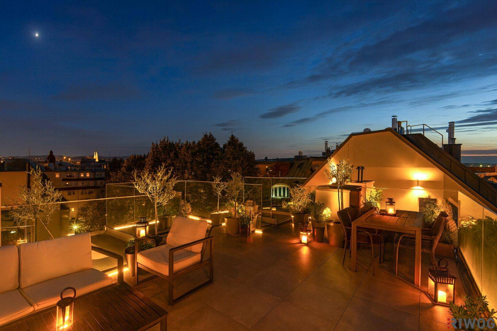 Eine stimmungsvolle Dachterrasse bei Nacht mit gemütlichen Sitzgelegenheiten und weitem Stadtblick.
