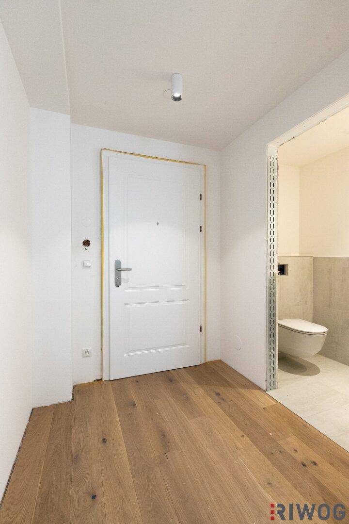 Eingangsbereich mit Holzboden und Zugang zu einem modernen Gäste-WC mit Wand-WC.