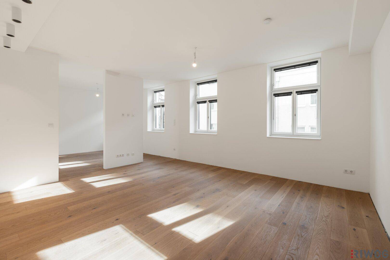 Lichtdurchfluteter Raum mit Holzboden und großen Fenstern, ideal für einen offenen Wohn- oder Essbereich.