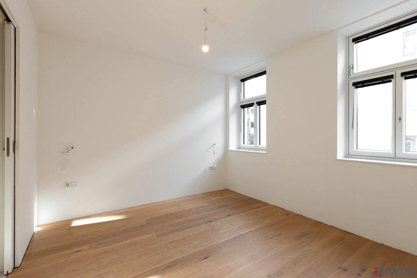 Helles Schlafzimmer mit Holzboden und großen Fenstern, bietet viel Platz für individuelle Einrichtung.