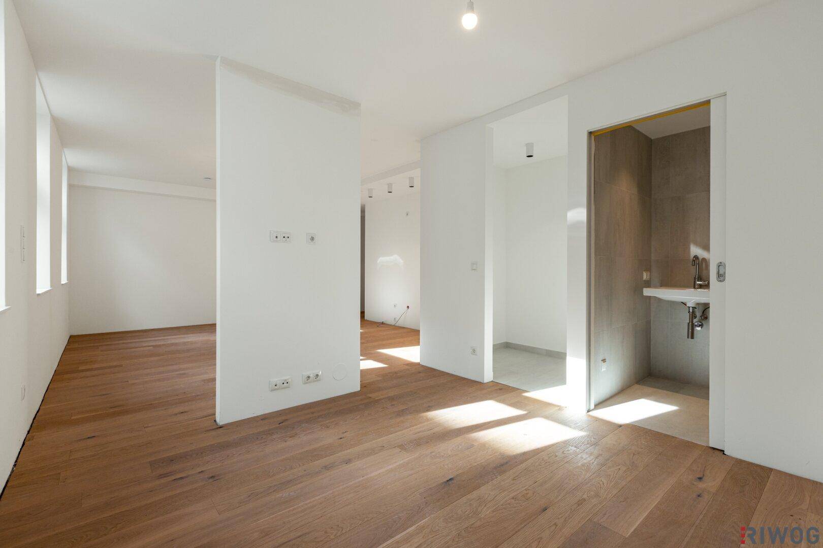 Heller Raum mit Holzboden und Zugang zu einem Badezimmer mit modernem Waschbecken.