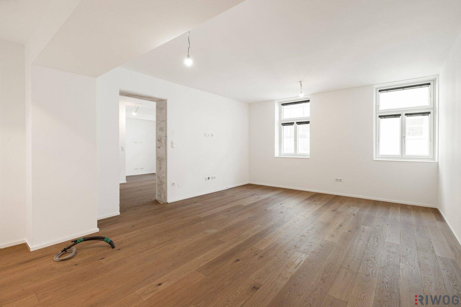 Geräumiges, leeres Wohnzimmer mit Holzboden und großen Fenstern, bereit zur individuellen Gestaltung.