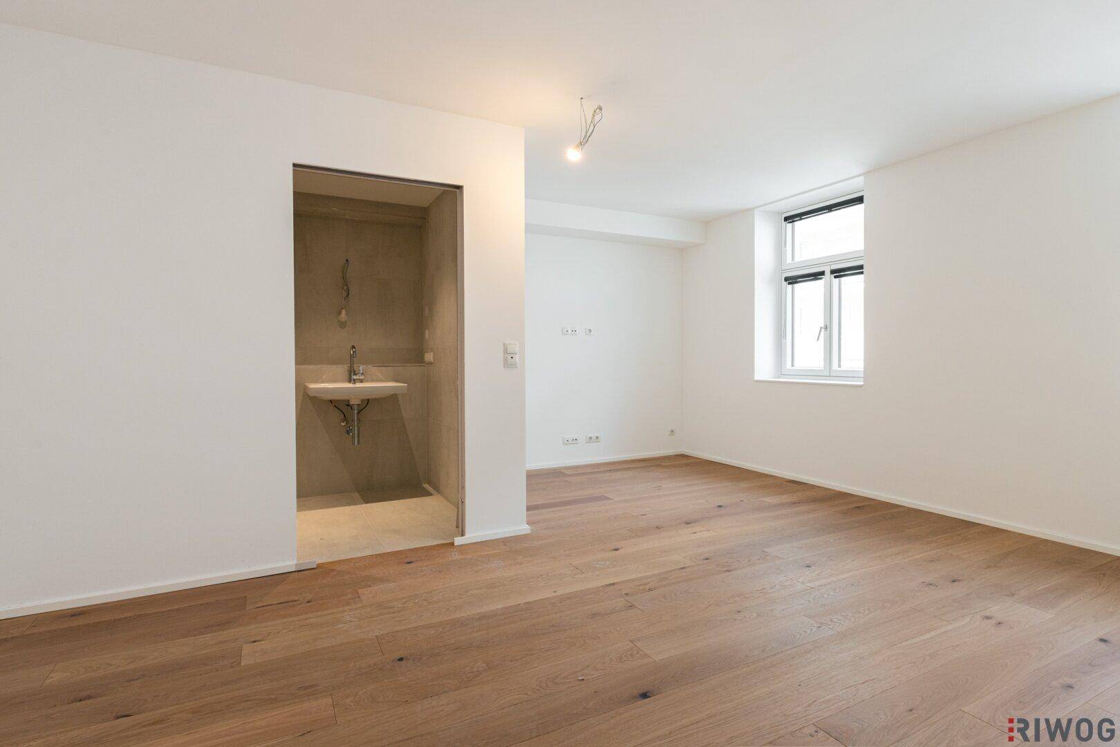 Helles, leeres Schlafzimmer mit Holzboden und offenem Waschbereich, ideal für moderne Wohnkonzepte.