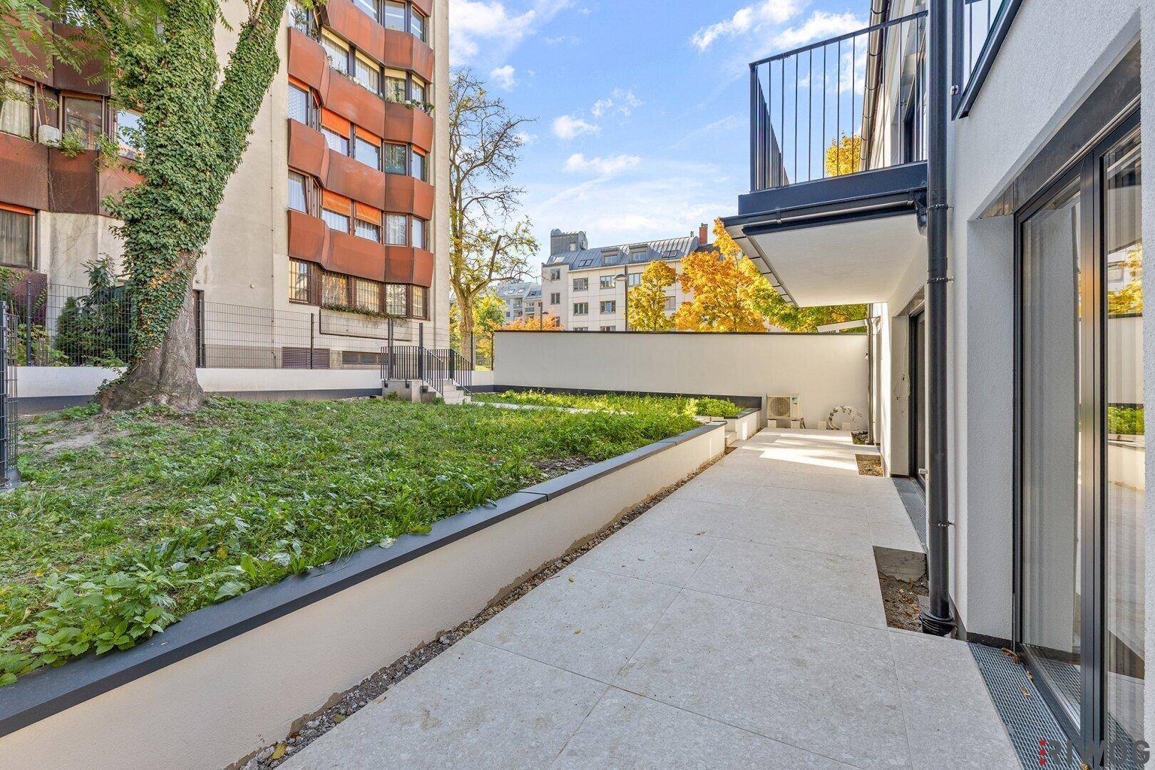 Gepflasterte Terrasse neben einem grünen Gartenbereich mit Bäumen und Sträuchern.