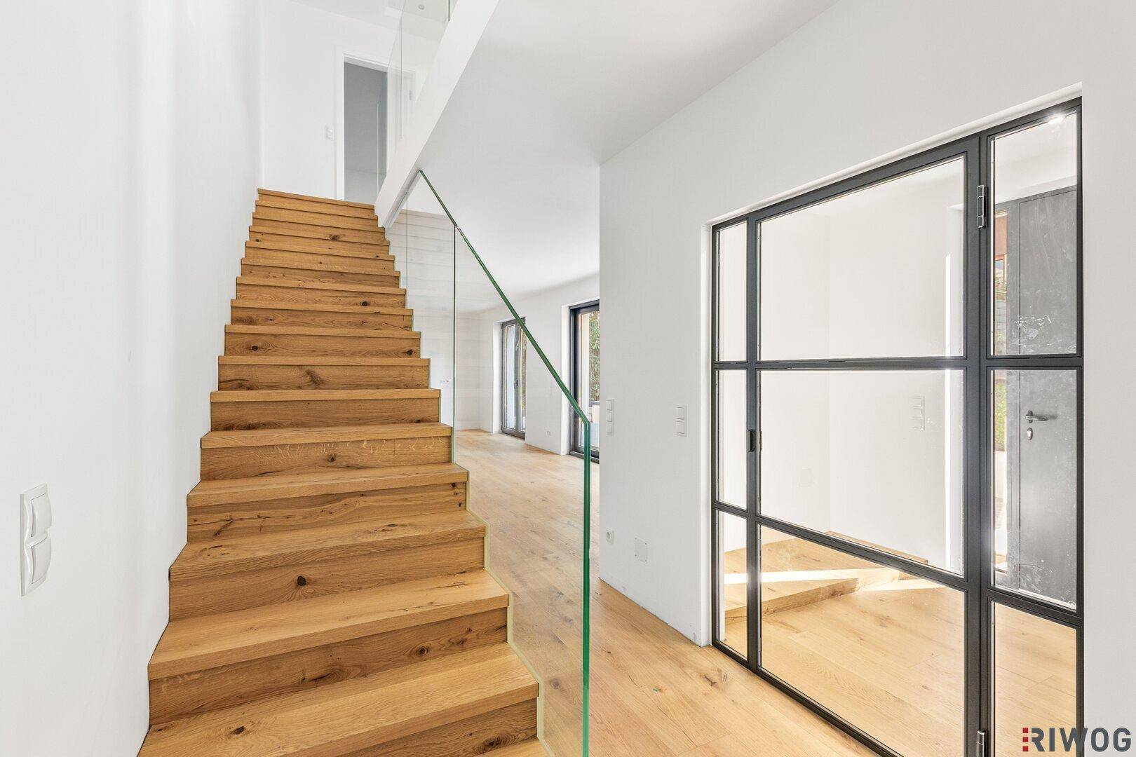 Moderne Holztreppe mit Glasgeländer und hellem Eichenparkettboden im Eingangsbereich.