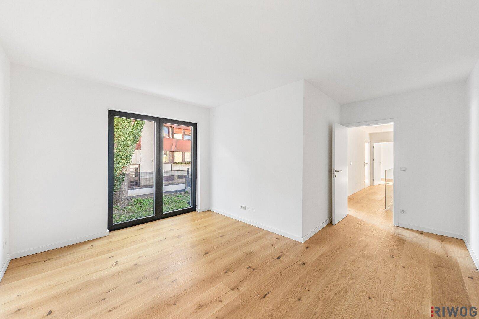 Helles Schlafzimmer mit Eichenparkettboden und großem Fenster mit Blick ins Grüne.
