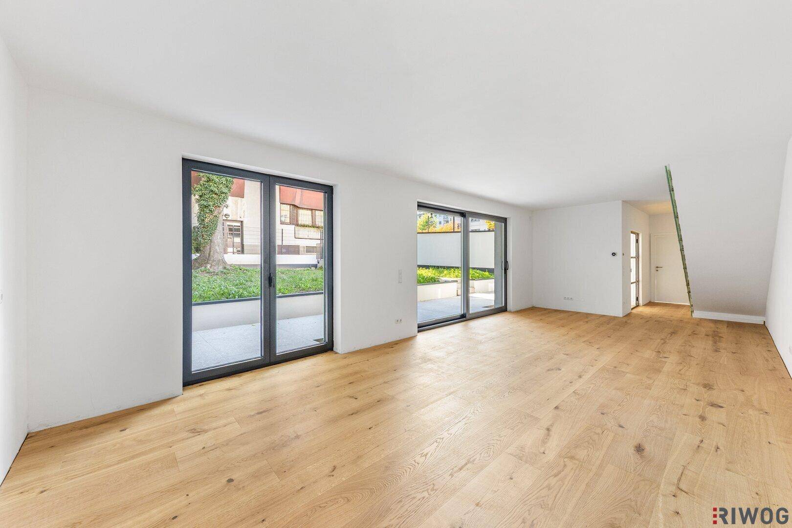 Heller, leerer Wohnbereich mit Eichenparkettboden und großen Fenstern zum Garten.