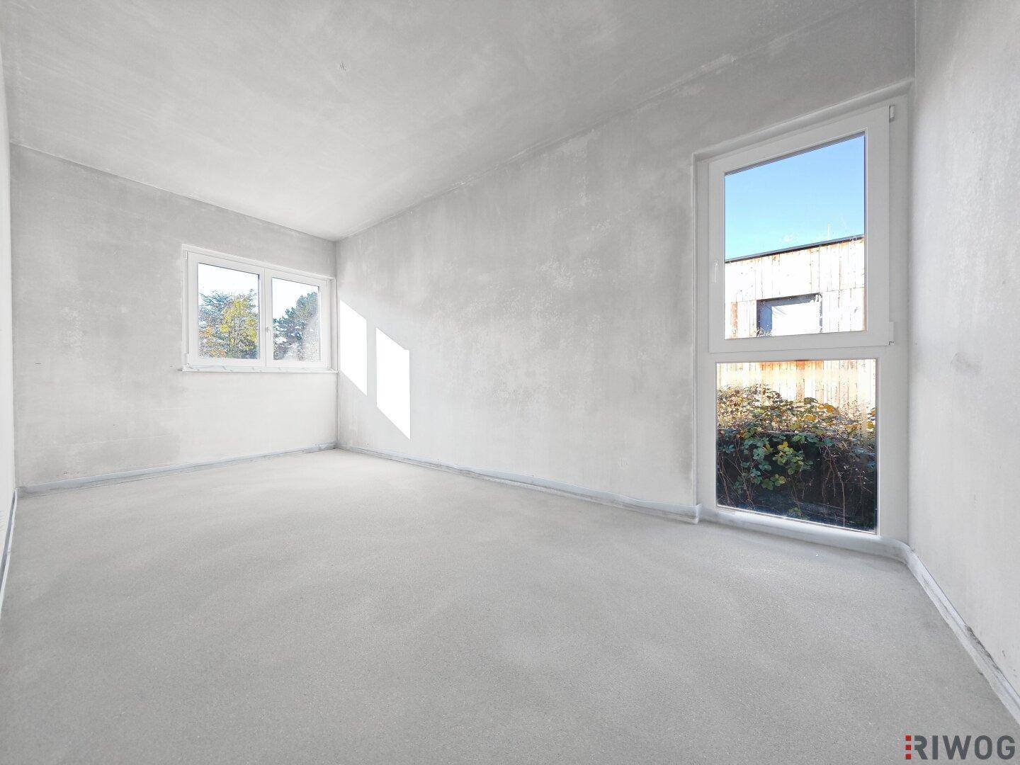 Helles, unfertiges Zimmer mit großen Fenstern und Blick ins Grüne, bereit für den Ausbau.