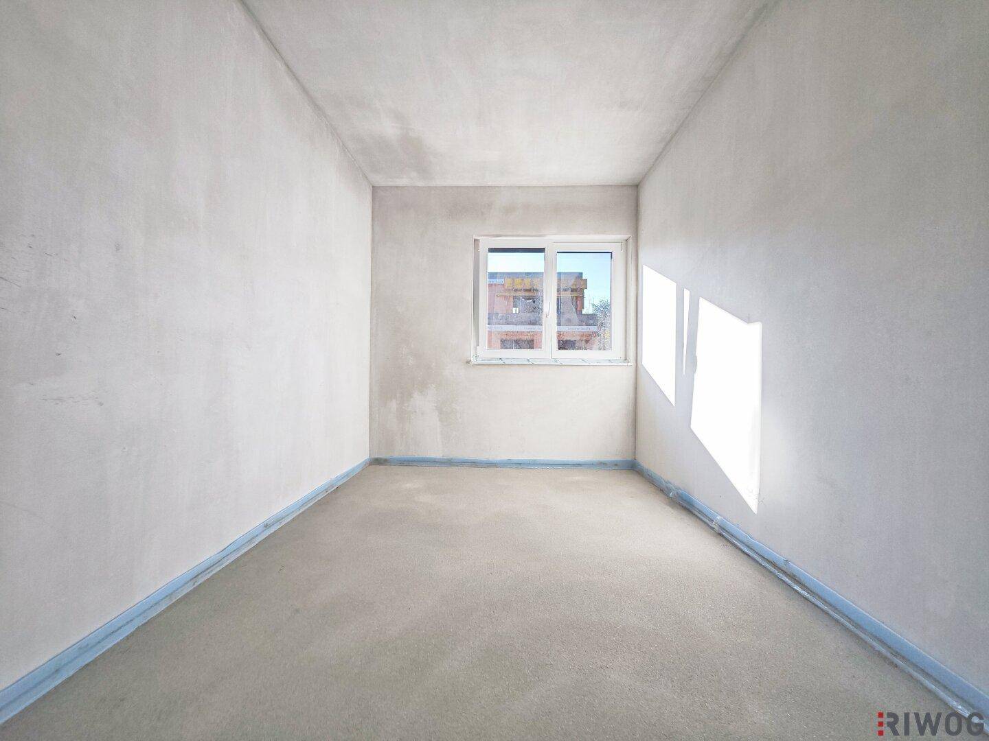 Einfacher, unfertiger Raum mit einem Fenster, das natürliches Licht hereinlässt.