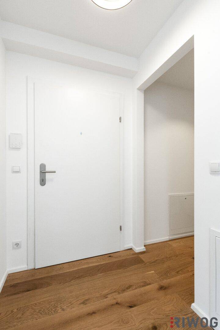 Heller Eingangsbereich mit Holzboden und weißer Tür, die in die Wohnung führt.
