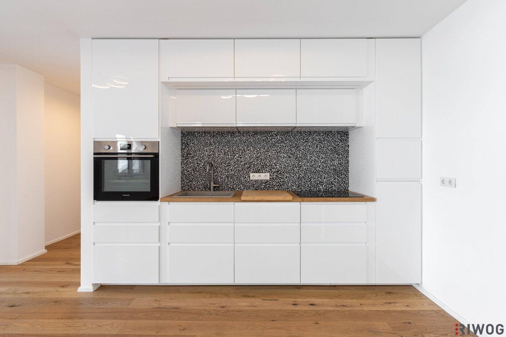 Moderne Einbauküche mit weißen Hochglanzfronten, Holzarbeitsplatte und integriertem Backofen.