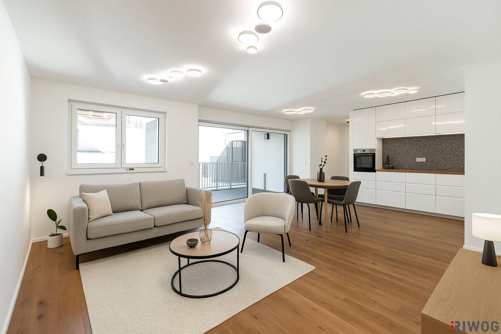 Helles, offenes Wohnzimmer mit integrierter Küche, Holzboden und Zugang zum Balkon.