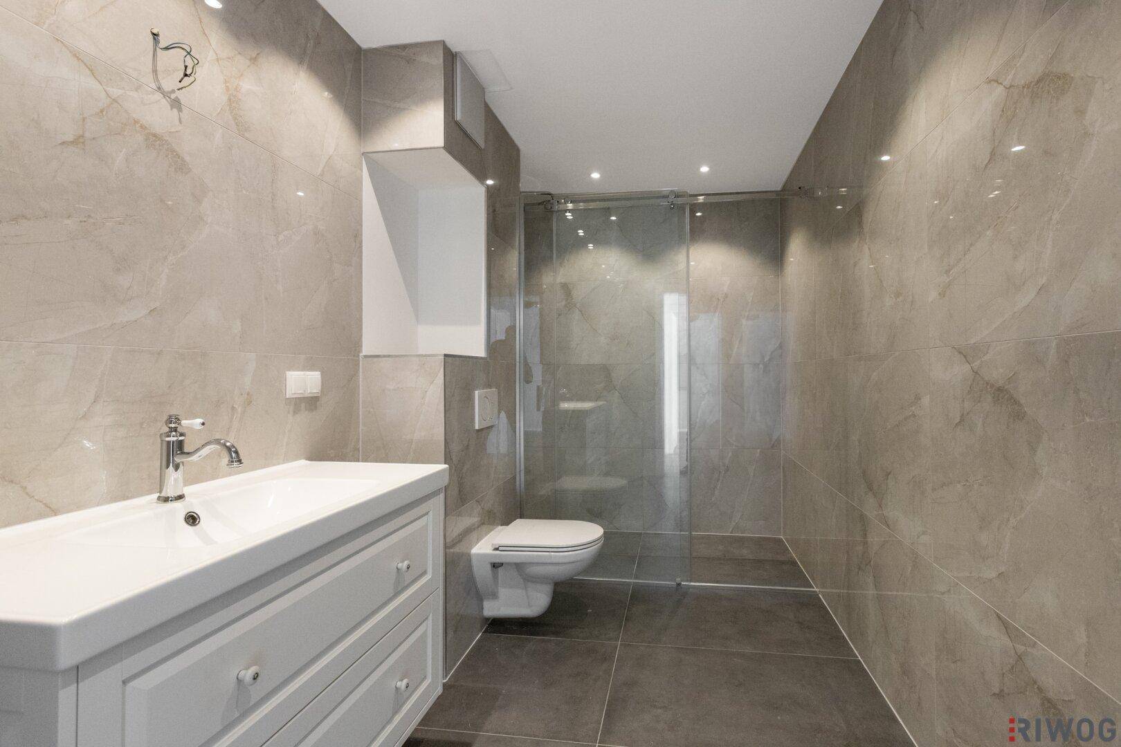 Modernes Badezimmer mit grauen Fliesen, begehbarer Dusche und Waschtischunterschrank.