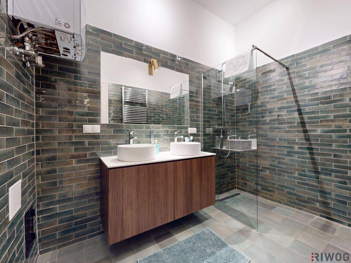 Modernes Badezimmer mit Doppelwaschbecken, großer Dusche und dunklen Wandfliesen.