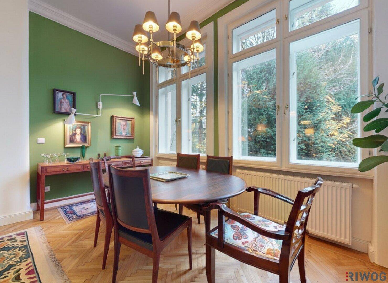 Heller Essbereich mit Holztisch, Stühlen und Blick ins Grüne durch große Fenster.