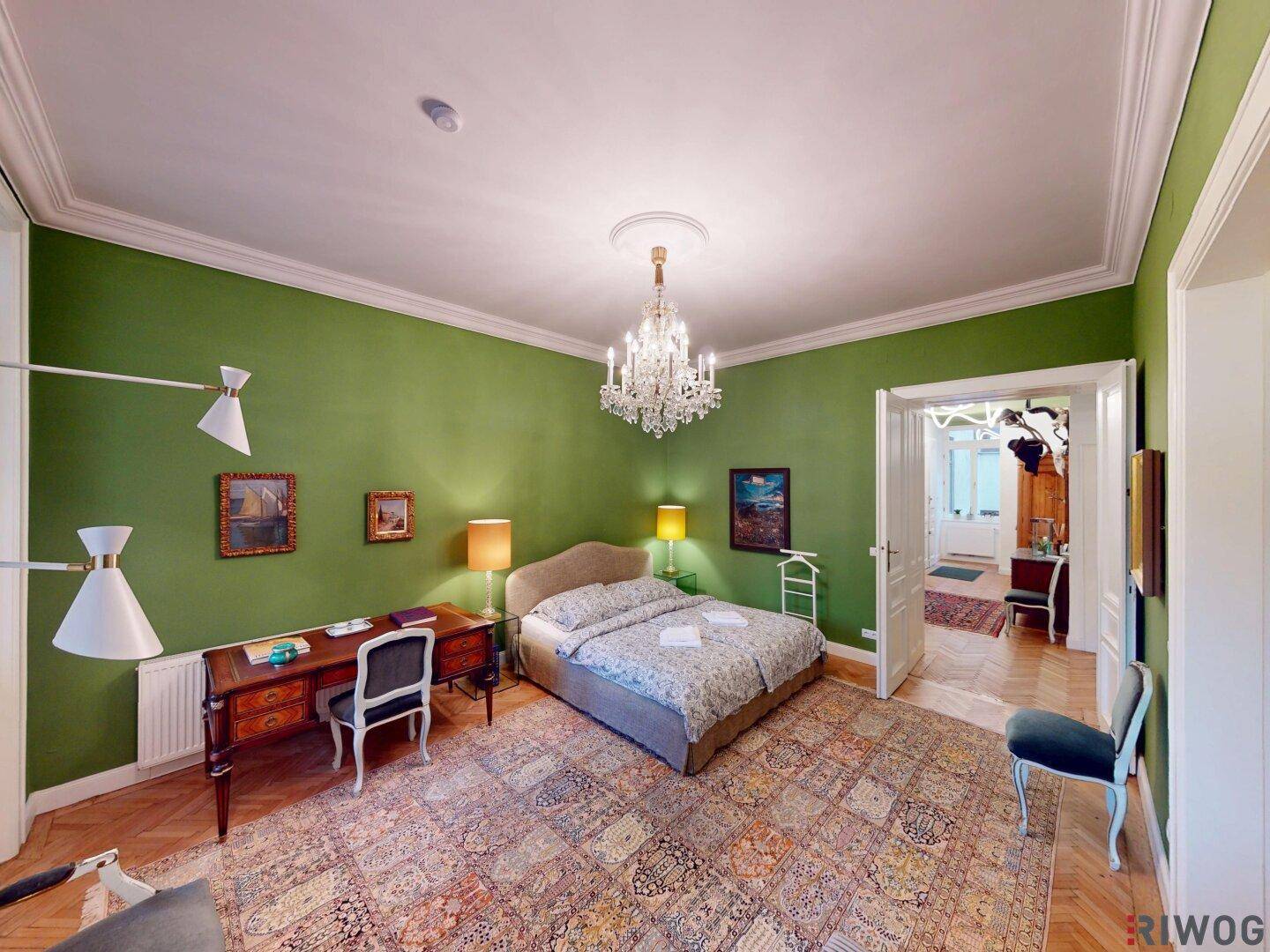 Helles Schlafzimmer mit Schreibtisch, Parkettboden und klassischem Kronleuchter.