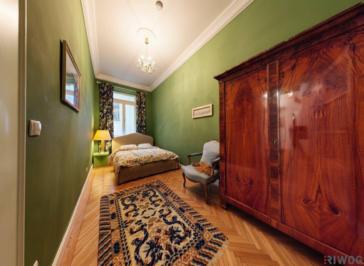 Gemütliches Schlafzimmer mit Parkettboden, grünen Wänden und großem Holzschrank.