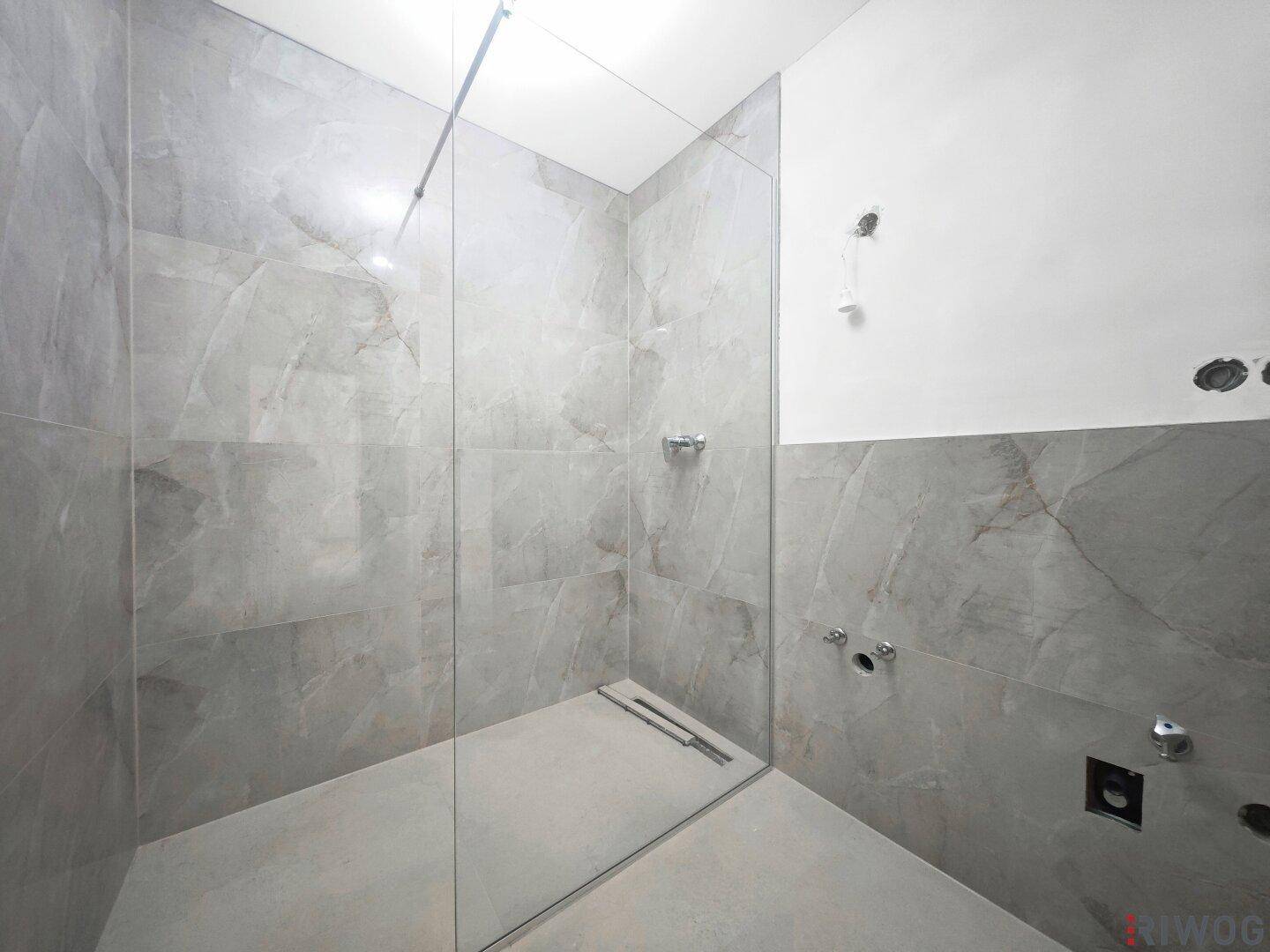 Modernes Badezimmer mit begehbarer Dusche und großformatigen grauen Fliesen, noch im Ausbau.