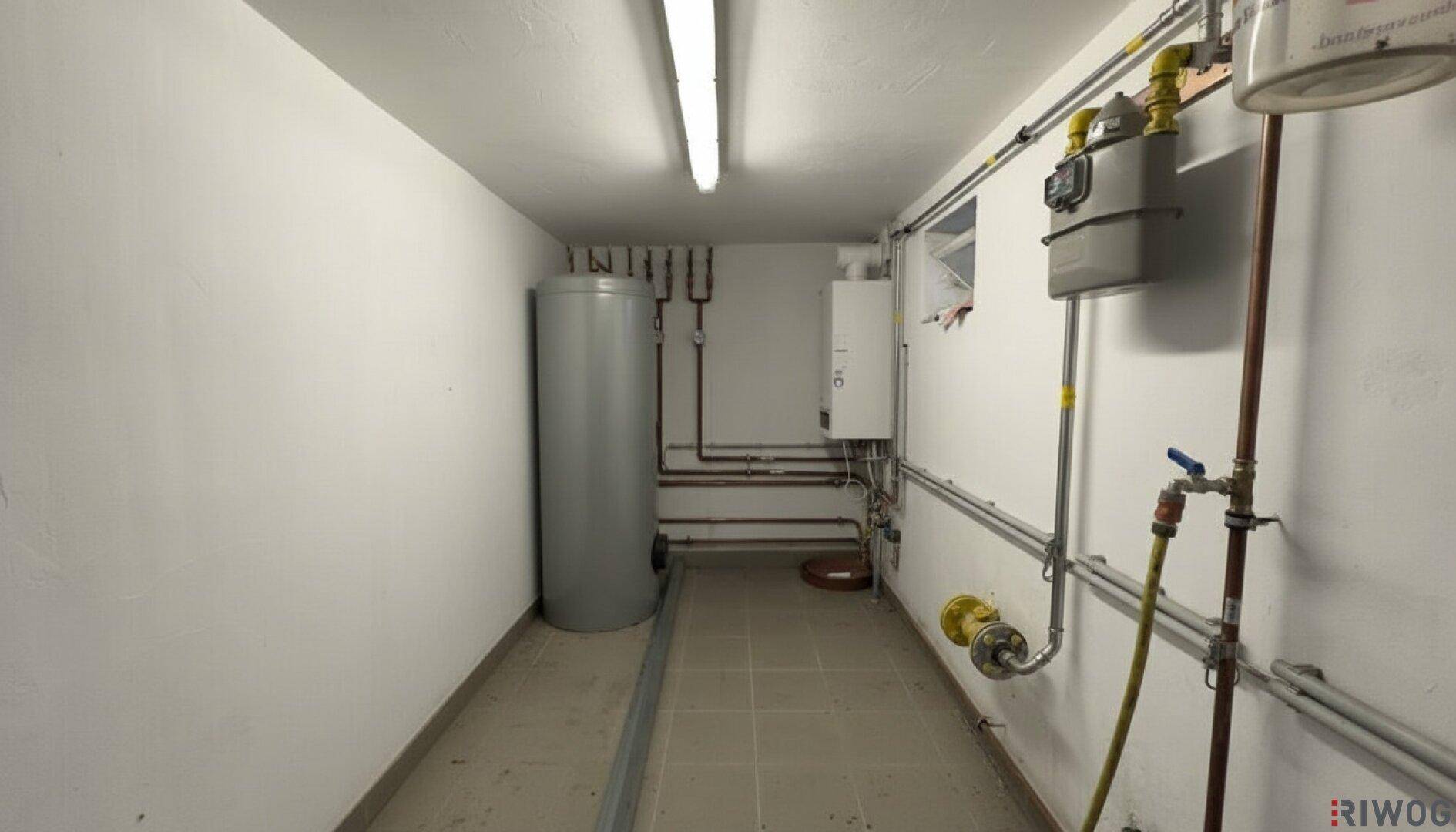 Heizungsraum mit Warmwasserspeicher, Gaszähler und sichtbaren Installationen an den Wänden.