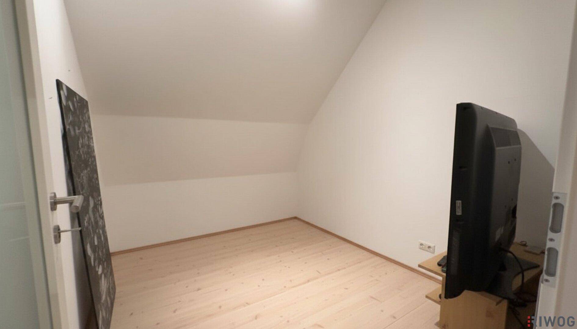 Leerer Raum im Dachgeschoss mit Dachschräge, Holzboden und einem Fernseher.