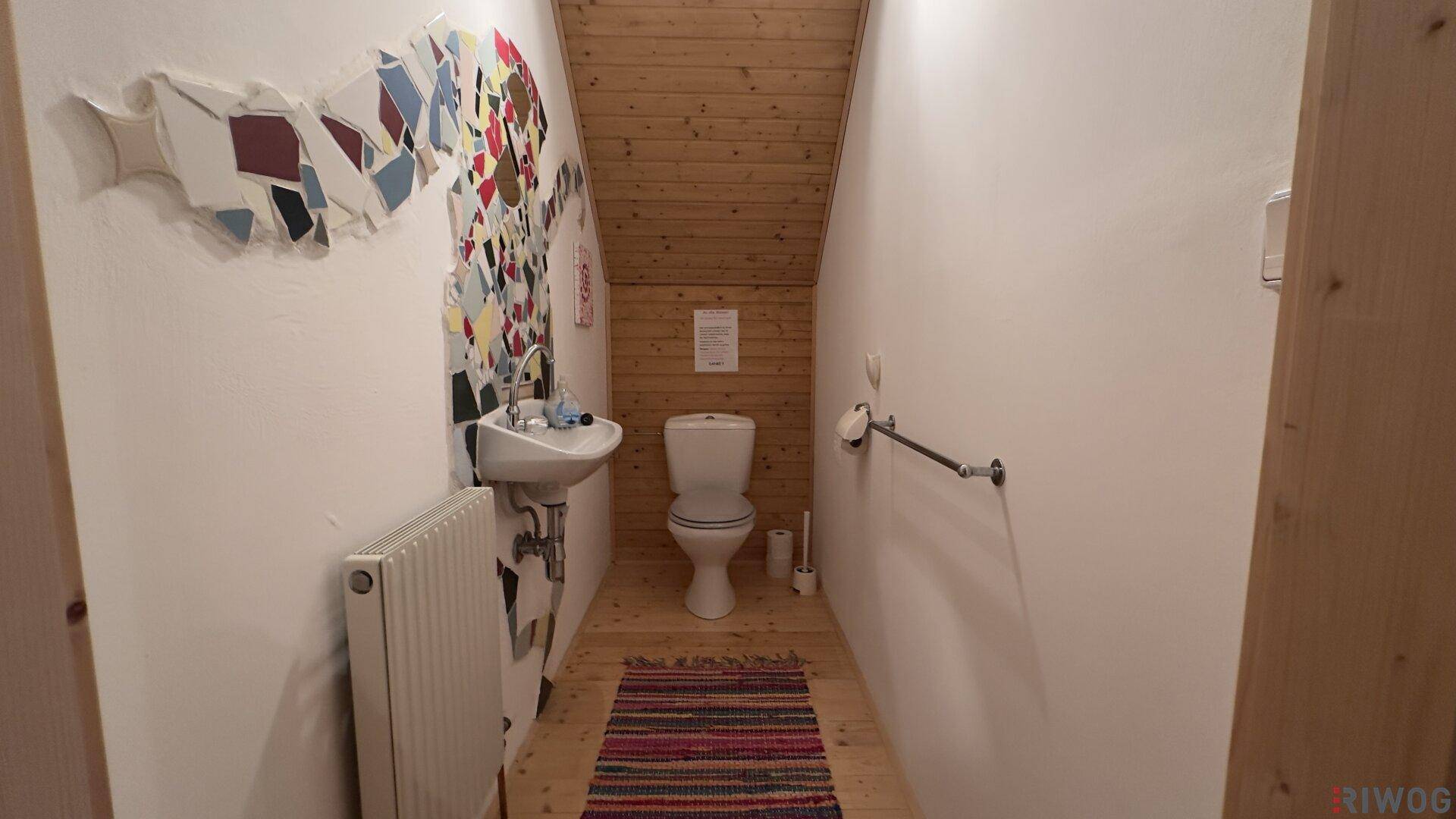 Kleine Gästetoilette mit Waschbecken, WC und Holzboden, dekoriert mit bunten Mosaiken.