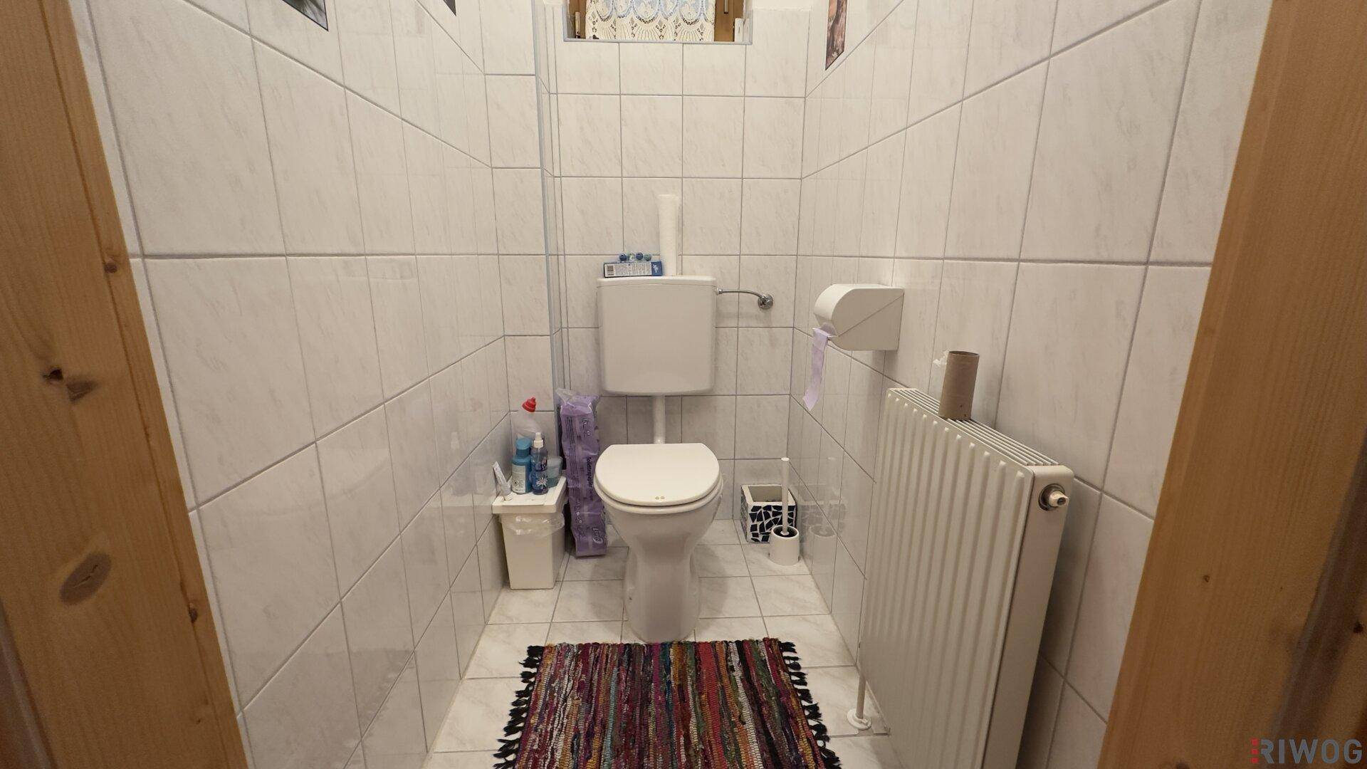 Kleine Gästetoilette mit weißen Fliesen, WC und Heizkörper, einfach und funktional.