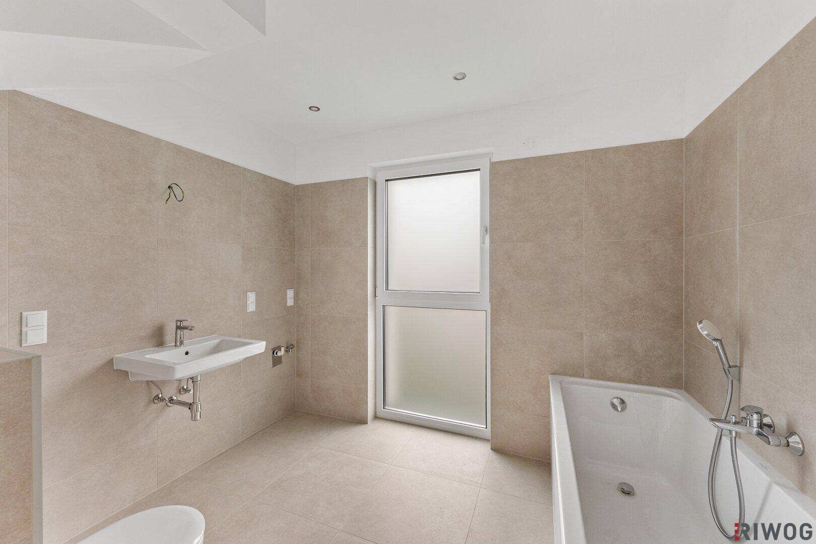 Geräumiges Badezimmer mit Badewanne, modernem Waschbecken und großem Fenster.