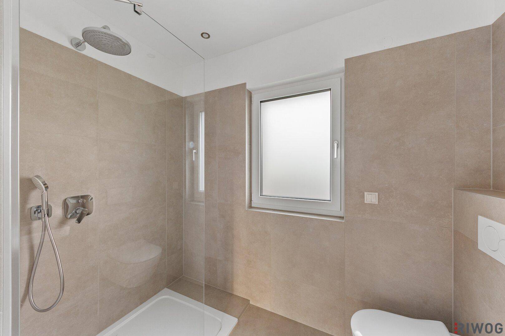 Modernes Badezimmer mit beigefarbenen Fliesen, Regendusche, Wand-WC und Fenster.