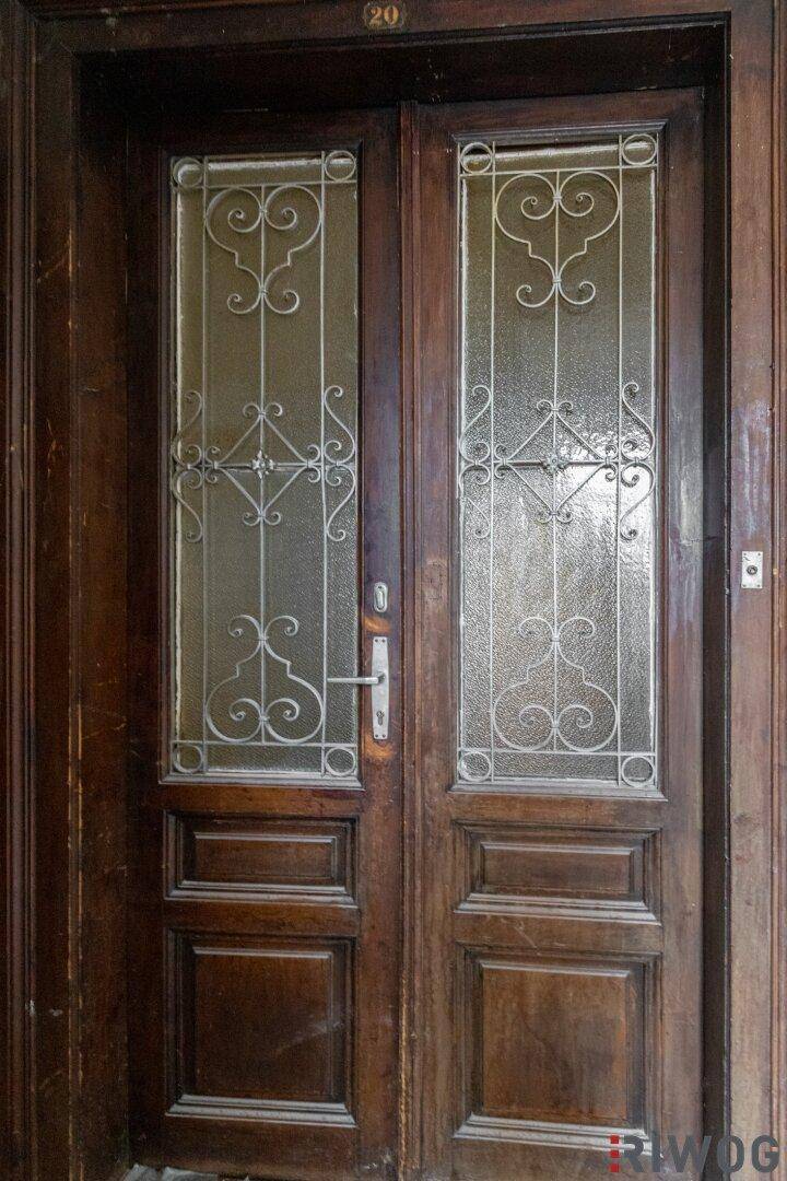 Historische Eingangstür aus Holz mit verzierten Glaseinsätzen und Metallgittern.