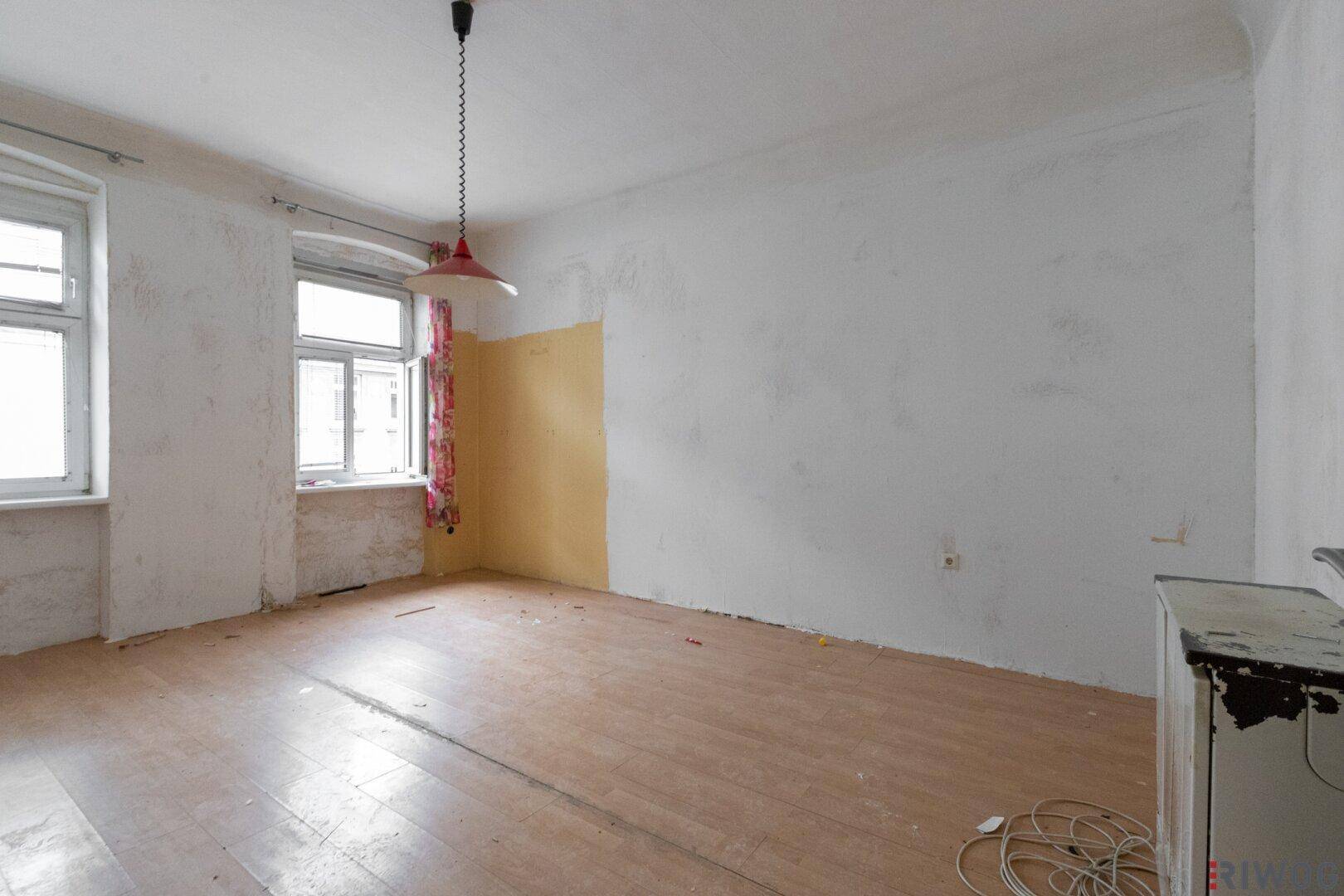 Geräumiger, unmöblierter Raum mit Holzboden und hellen Fenstern, bereit zur Renovierung.