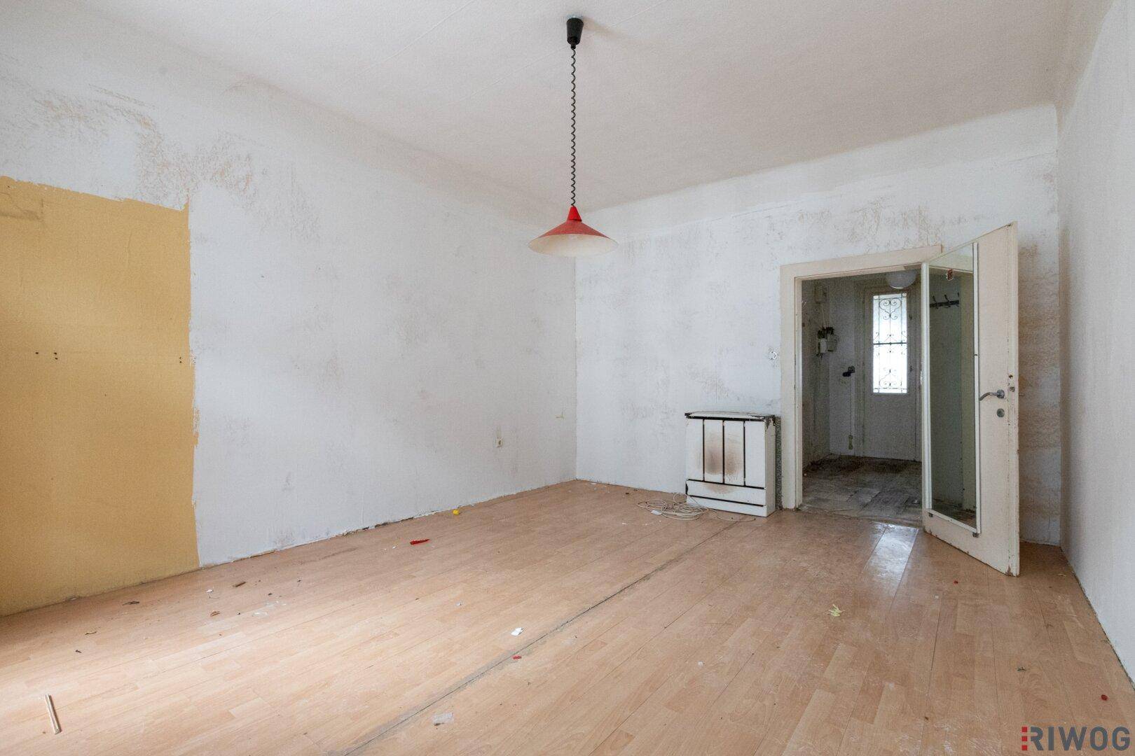 Leerer Raum mit Holzboden und einem Durchgang zu einem weiteren Zimmer, renovierungsbedürftig.