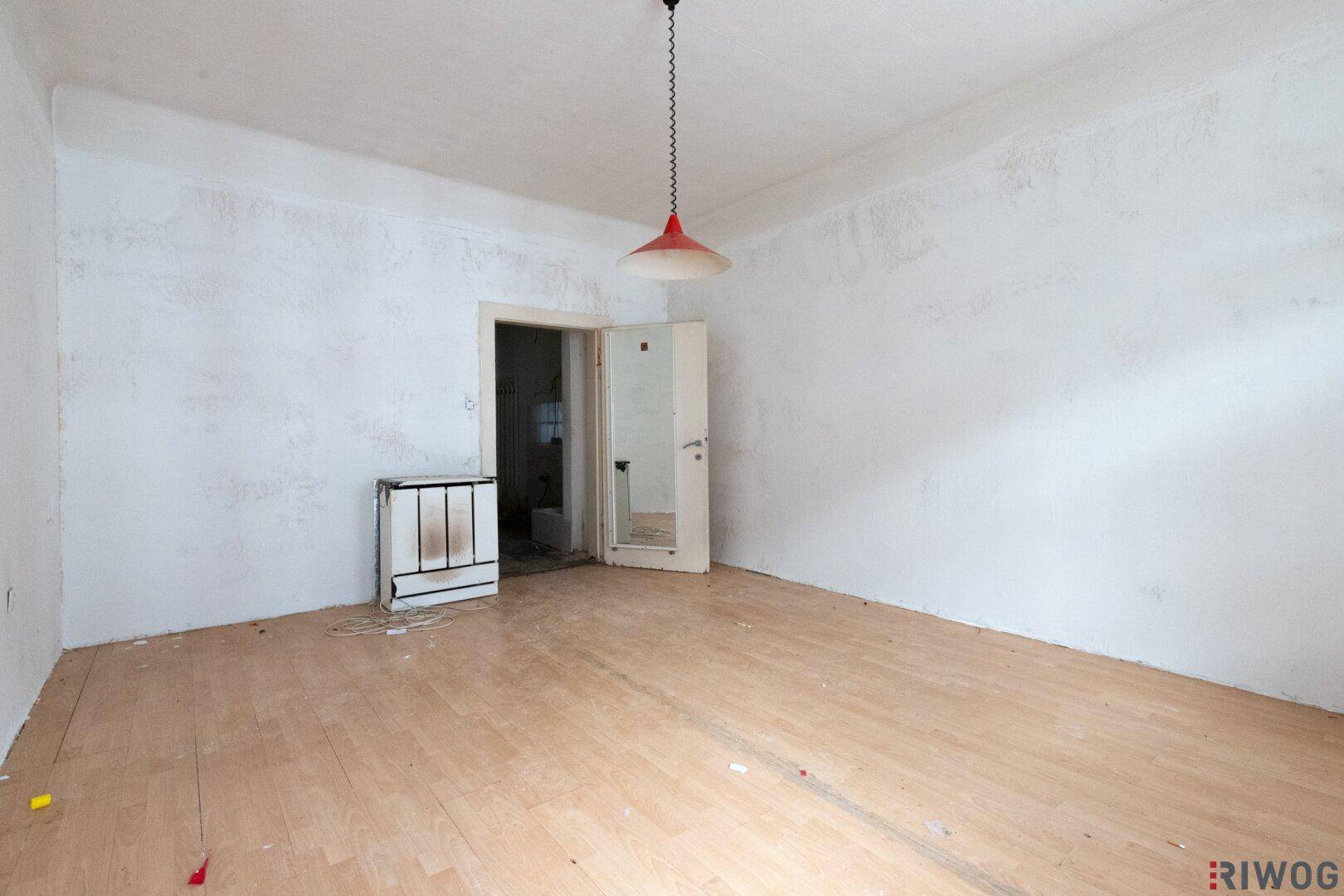 Unmöblierter Raum mit Holzboden und weiß gestrichenen Wänden, die eine Auffrischung benötigen.