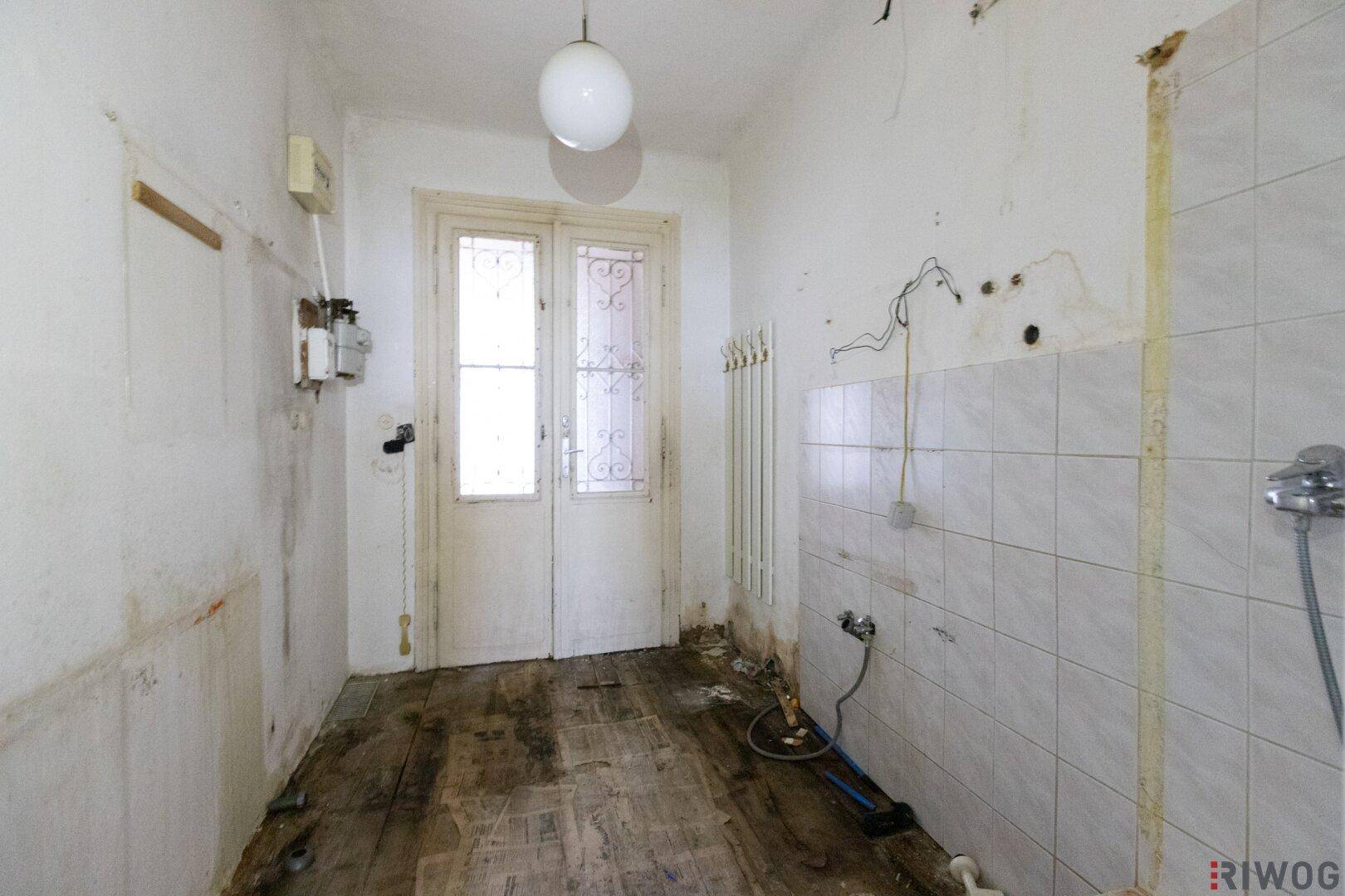 Renovierungsbedürftiges Badezimmer mit alter Tür und Heizkörper, bereit für eine Neugestaltung.