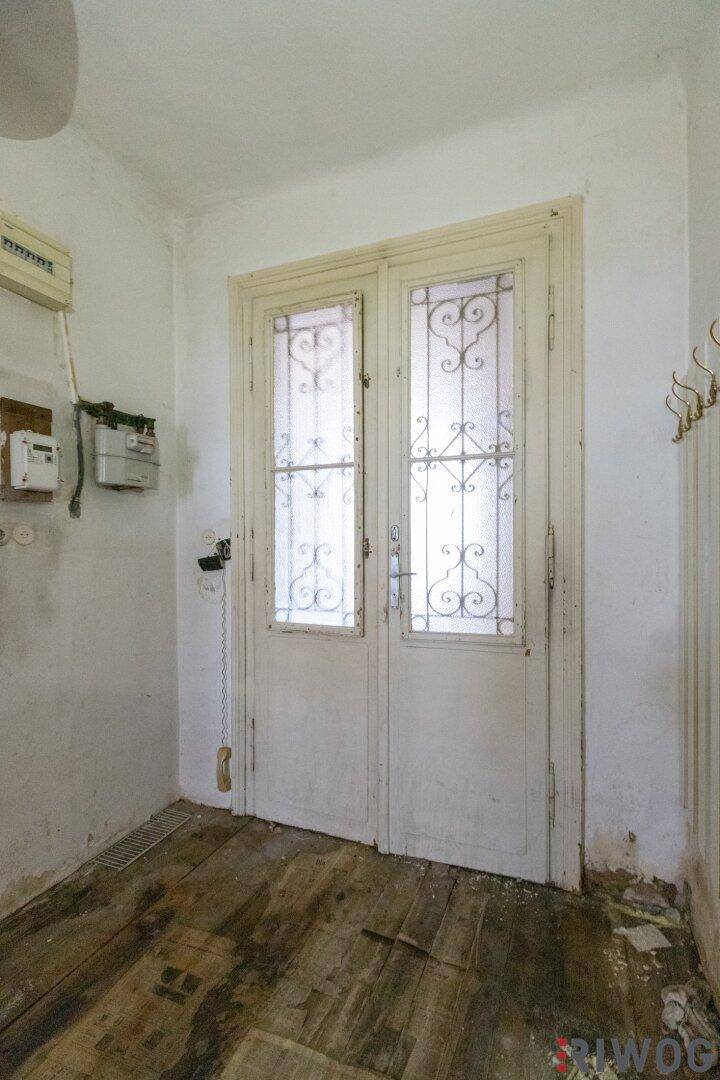 Eingangsbereich mit alter Holztür und sichtbaren Installationen, die eine Renovierung benötigen.