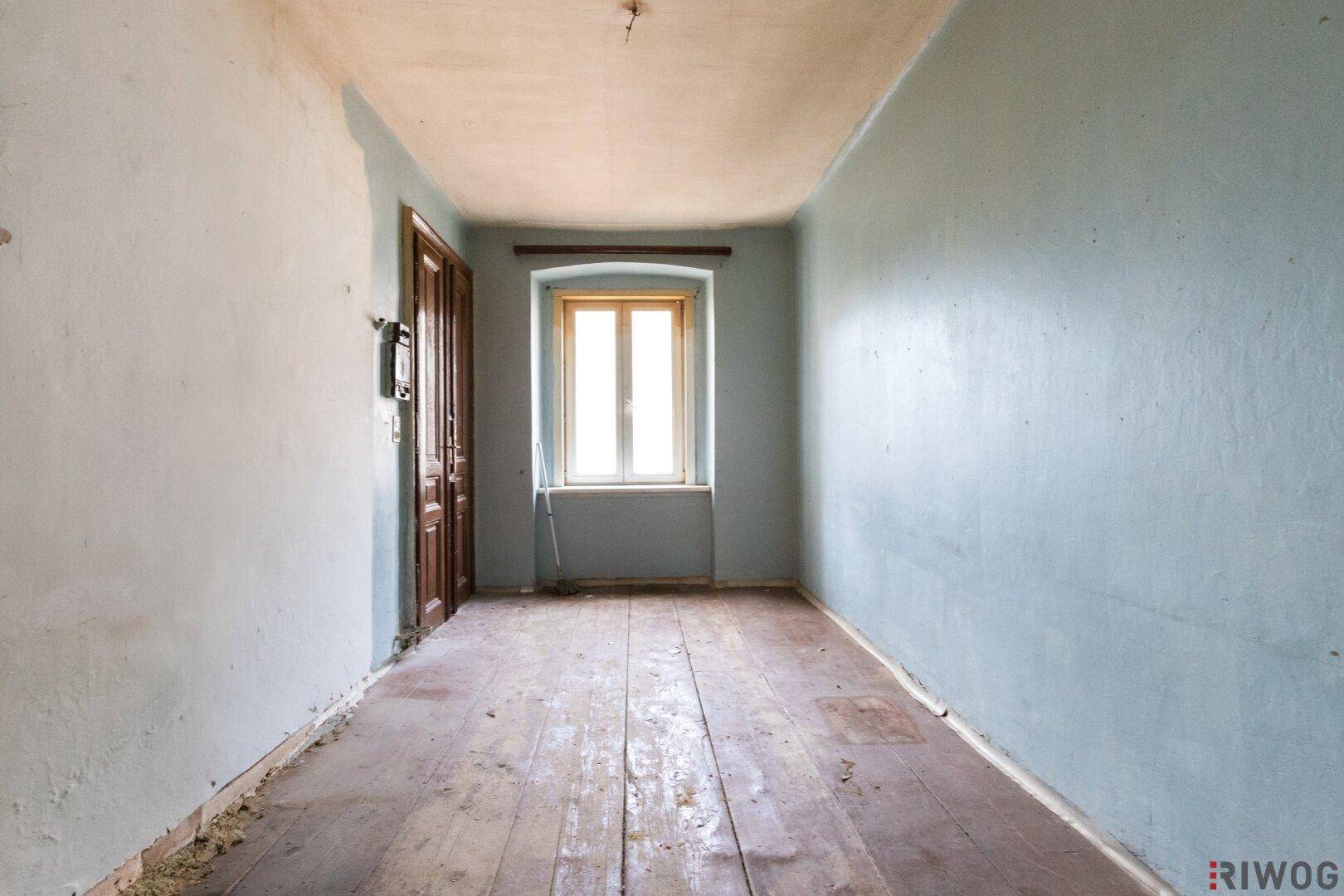 Leeres Zimmer mit blauen Wänden, Holzdielen und einer Holztür, bereit für eine Renovierung.