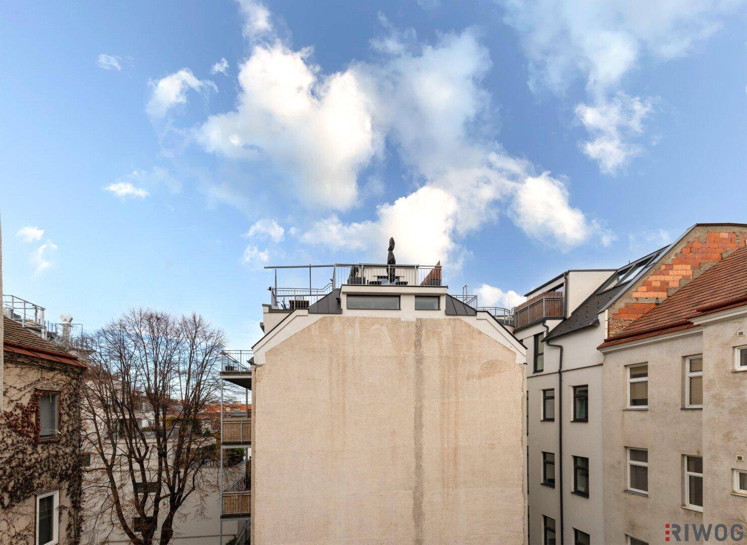 Rückansicht eines Gebäudes mit mehreren Fenstern und einem Flachdach mit Dachaufbauten.