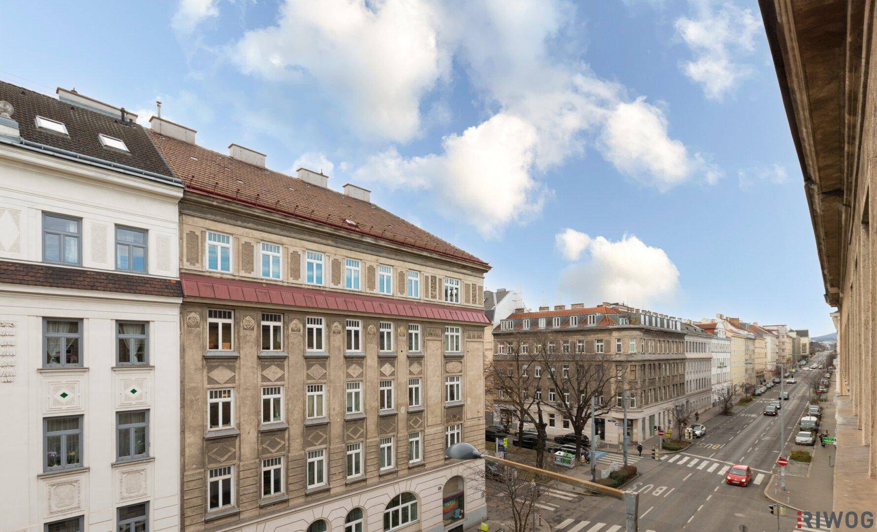 Panoramablick von oben auf eine städtische Straße mit Altbauten und Grünflächen in der Ferne.
