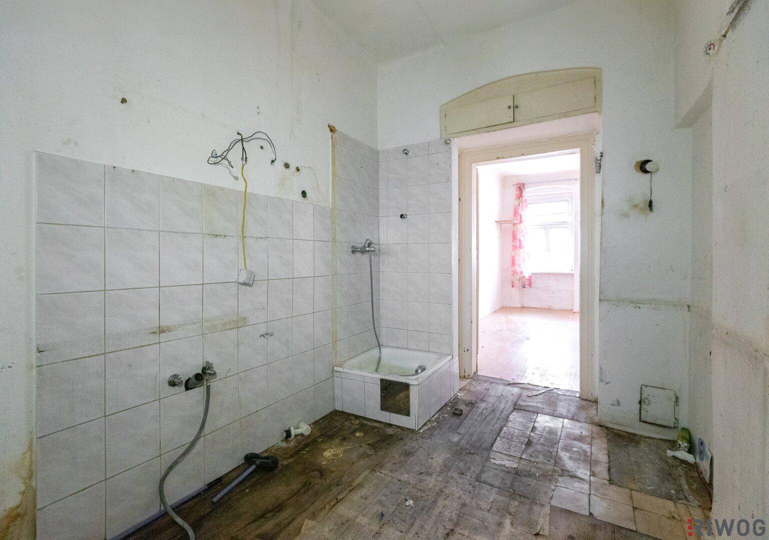 Badezimmer in schlechtem Zustand mit Fliesenwänden, Holzdielen und einer kleinen Badewanne.