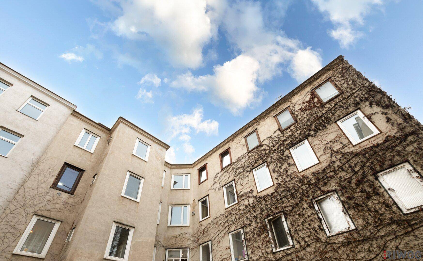 Blick in den Innenhof eines Altbaus mit bewachsenen Fassaden unter blauem Himmel.