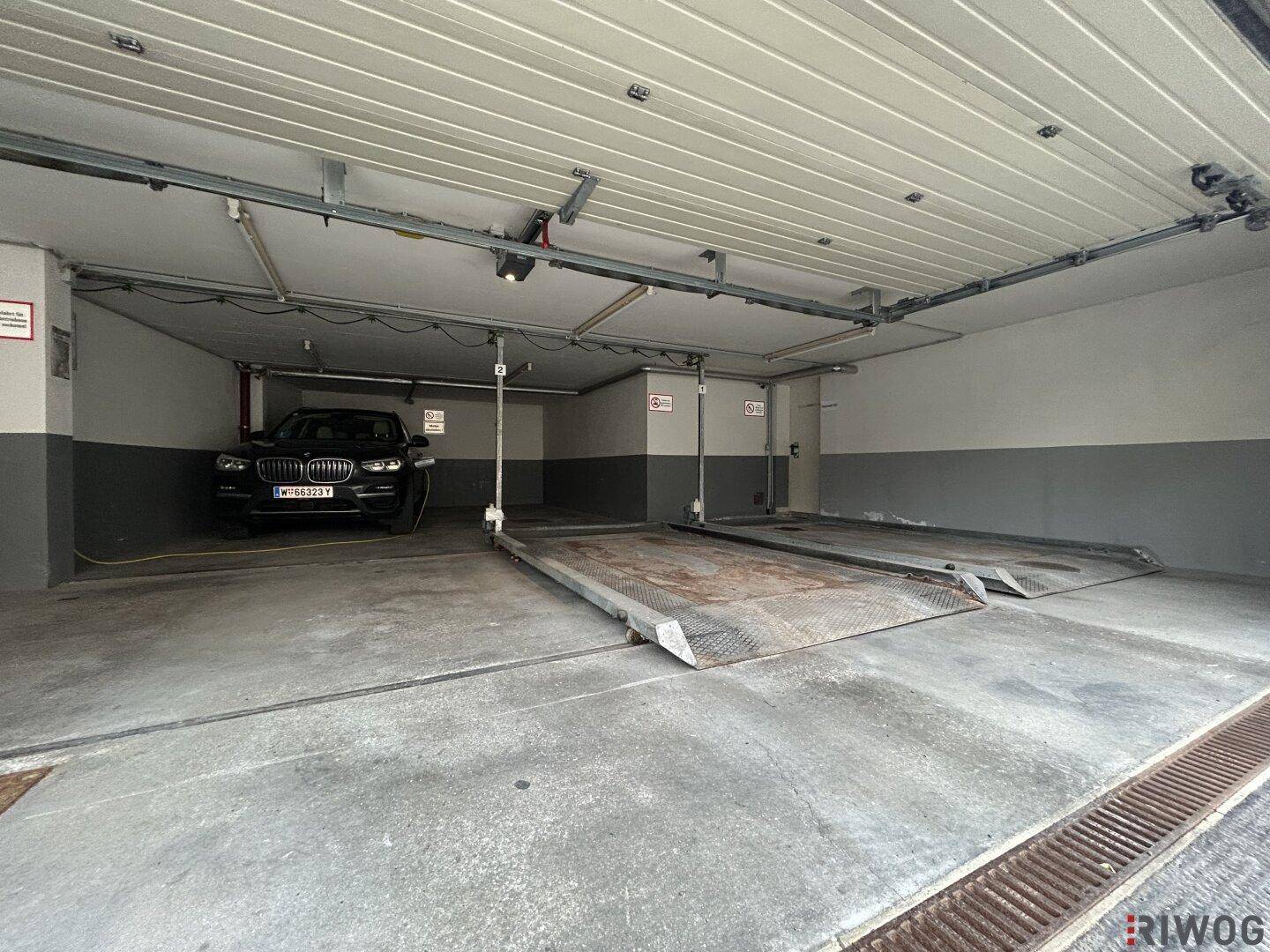 Innenansicht der Tiefgarage mit zwei Autohebebühnen und einem geparkten Fahrzeug auf einer Plattform.
